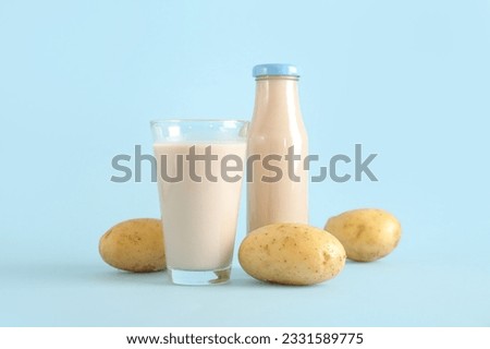Bottle and glass of tasty potato milk on blue background