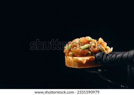 Salmon and avocado tartar in hand on the black background