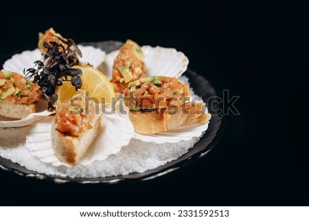 Cold fish appetizer Salmon and avocado tartar on a black plate on a black background