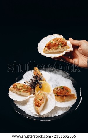 Salmon and avocado tartar in shell which is held in the hand over the dish