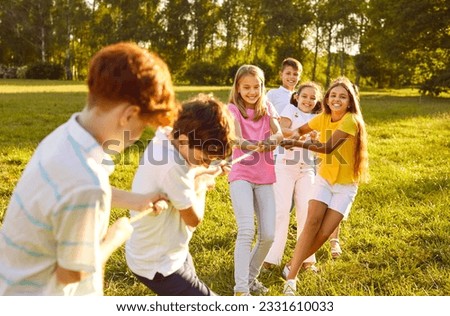 Happy children play games in park on sunny summer day. Cheerful kids meet on green field or meadow, hold rope, play tug of war, compete with each other, enjoy challenge, make effort. Teamwork concept Royalty-Free Stock Photo #2331610033