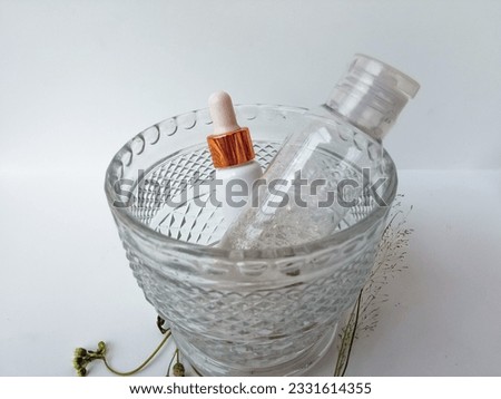 Serum and Makeup remover in a plastic white bottle in a transparent bowl on a white background with flowers.  Natural organic beauty liquid products. Natural skincare for beautiful healthy skin