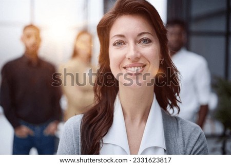 Portrait of a young woman standing in an office with colleagues in the background.