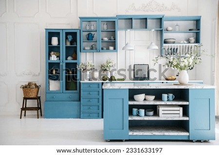 Kitchen in scandinavian style with island table, blue furniture and modern kitchenware. Bright interior with white walls and floor. Vase with flowers on marble countertop. Royalty-Free Stock Photo #2331633197