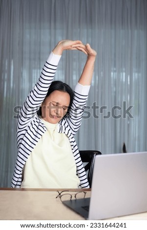 Woman stretching arm raised sitting incorrect position home office desk tired from work body stress