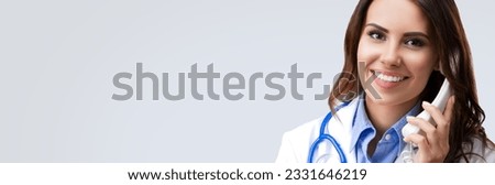 Happy smiling female doctor on phone, isolated over grey color background. Medical call center concept picture.