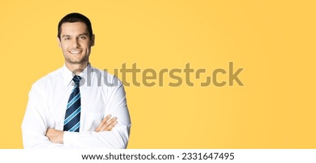 Portrait of happy smiling young brunette businessman in white shirt and blue tie, standing in crossed arms pose, isolated over orange yellow colour background with copy space. Confident business man.