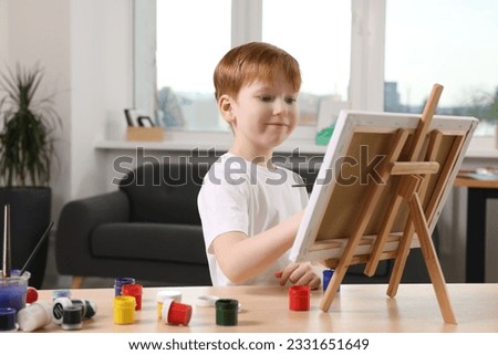 Little boy painting at table in studio. Using easel to hold canvas