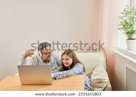 Granddaughter helping grandpa to make on line communication on laptop, listening to modern music, old man with his granddaughter using laptop making video call Royalty-Free Stock Photo #2331651803