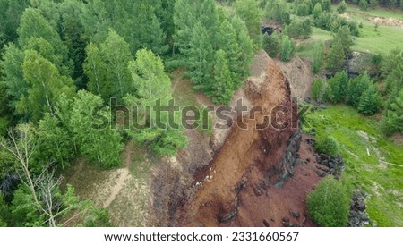 Aerial along view of the long-extinct volcano vent surrounded by a small coniferous forest and meadows with cows and horses, high mountain range on a rainy summer day, color picture, down