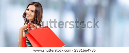 Image of shopping woman. Happy smiling girl holding grocery bags, on blurred modern mall background. Copy space for some text. Brunette model - consumerism, sales and shopaholic concept picture. 