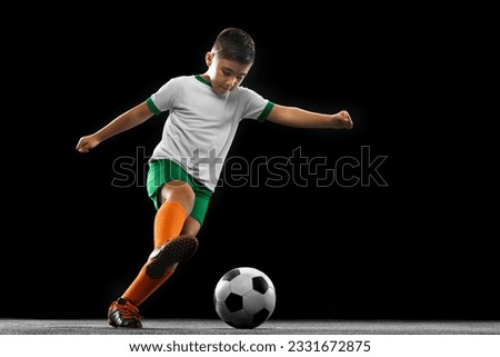 Match preparation. Portrait of boy, child, football player in uniform training, dribbling ball isolated over black background. Concept of action, team sport game, energy, vitality. Copy space for ad.