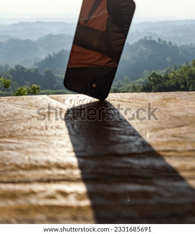 Shadow of a mobile phone on its corner stands in a wooden bench, the shadow falls beautifully on the front