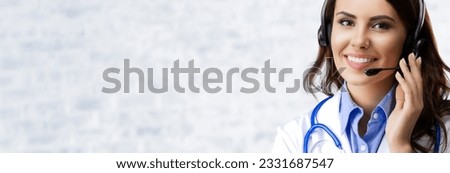 Portrait of happy smiling female doctor in headset, over white brick loft wall background, with empty copy space area. Brunette woman at medical call center concept picture.