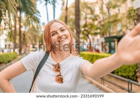 Happy optimistic girl enjoys free time and walking in city makes selfie poses against summer palms has fun during daytime, adventure vacation in Valencia, Spain. Tourism and travel concept. 