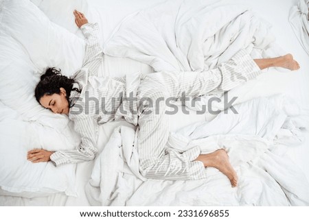 Beautiful brunette woman lies on her stomach on her bed in a star pose. She sleeps on her day off after a hard week at work. Inability to wake up and get out of bed is a sign of depression or illness Royalty-Free Stock Photo #2331696855