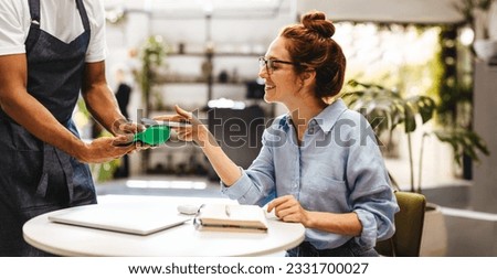 Female customer using NFC technology to pay her bill, scanning her smartphone on a payment terminal to complete the transaction. Happy woman using a cashless and contactless payment method in a cafe. Royalty-Free Stock Photo #2331700027