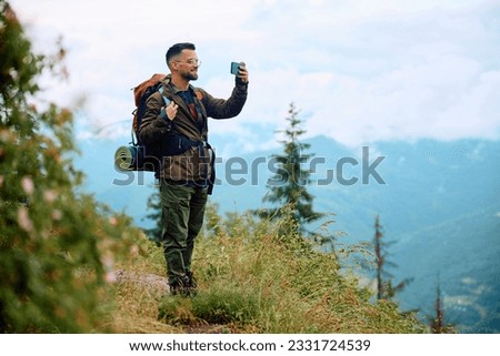 Happy backpacker taking pictures with smart phone while hiking in the mountains. Copy space.