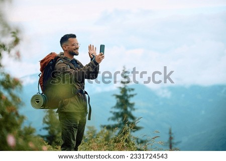 Happy backpacker greeting someone vie video call while hiking in the mountains. Copy space.