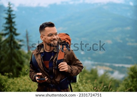 Happy hiker with smart phone walking up the hill during a rainy day. Royalty-Free Stock Photo #2331724751
