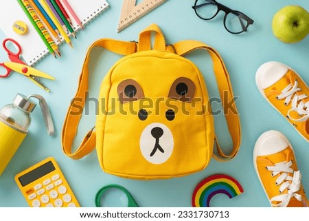 Nurturing bright minds. Overhead shot of a yellow child's rucksack with cartoon bear print packed with assorted colorful school materials and pair of shoes on a soft blue background Royalty-Free Stock Photo #2331730713