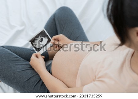 pregnant woman is looking at an ultrasound photo of fetus. Mother gently touches the baby on stomach. Happy, family, growth, pregnancy, enjoyment , prepare newborn, take care, healthcare, tummy.