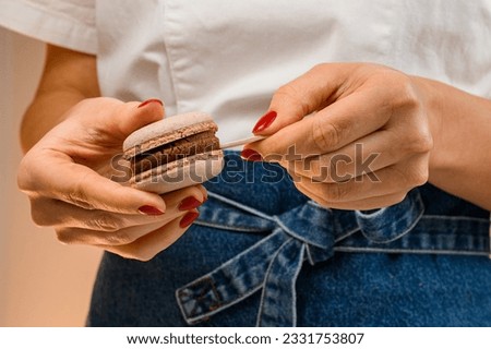 Woman confectioner's hands connecting two shells of macarons with chocolate ganache and puts wooden ice stick between them, close up view. Home made sweets.