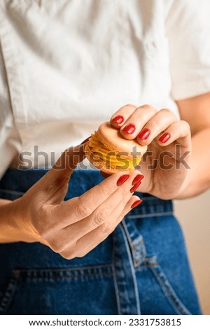 Woman confectioner's hands with red manicure connecting two halves of macarons, decorated with ganache. Home bakery concept