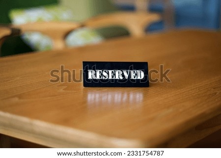 "Reserved", a sign placed on a black plastic plaque and placed on a wooden table in a cafe which is usually used as a sign that the table has been reserved.