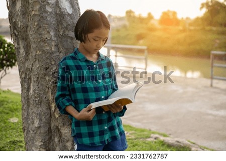 Cute little girl reading book on tree in park.SSTKHome