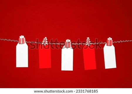 Festive red and white tags hanging from silver tinsel line on a red background