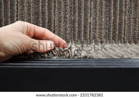 Person showing frayed carpet coming loose on stairstep, stair nosing or stair edging. High traffic staircase with commercial carpet damage by the edge, causing tripping hazard. Selective focus. Royalty-Free Stock Photo #2331782381