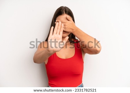 young adult pretty woman covering face with hand and putting other hand up front to stop camera, refusing photos or pictures