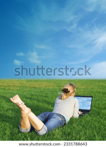 A girl using a laptop in a field.