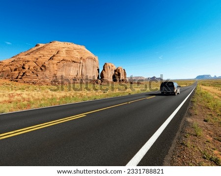 Sport utility vehicle on open highway in scenic desert landscape with butte land formation.
