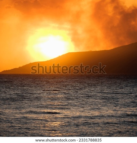 Sun setting behind mountain with ocean at Maui, Hawaii.