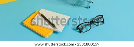 Smartphone, stationery, glasses and shopping cart over blue table
