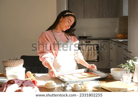 Lifestyle, cooking and freelance concept: Young woman baking cookies standing in her apron in kitchen at home. High quality photo