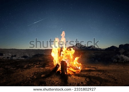Exploring the wilderness in summer. A glowing camp fire at dusk providing comfort and light to appreciate nature, good times and the night sky full of stars. Photo composite.
