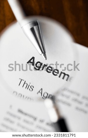 Magnifying glass over agreement paperwork and pen Royalty-Free Stock Photo #2331811791