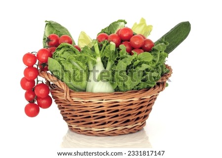 Rustic wicker basket of fresh salad vegetables, over white background.