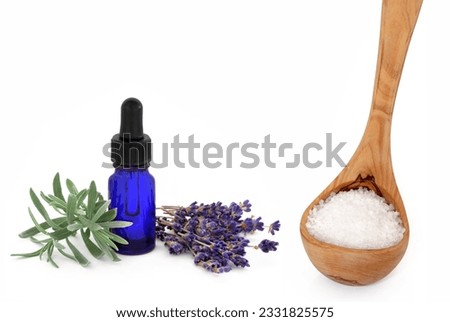 Lavender herb flowers and leaf sprig with an aromatherapy essential oil glass dropper bottle and wooden ladle with sea salt, over white background.