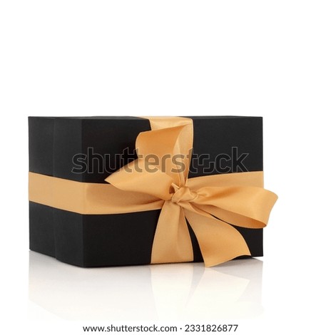 Black gift box with gold satin ribbon and bow, isolated over white background with reflection.