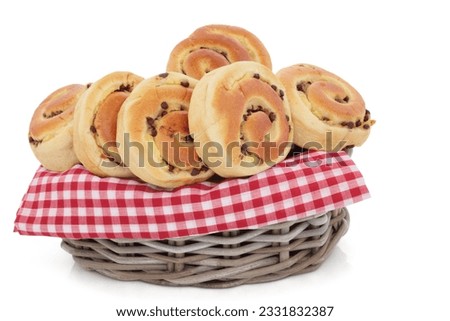 Chocolate chip brioche buns in a rustic wicker basket with a check picnic cloth over white background.