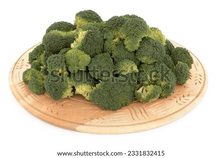Broccoli florets on a carved wooden chopping board against white background.