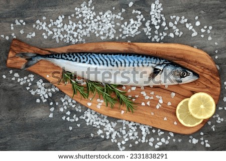 Mackerel fish health food on an olive wood board with course salt, rosemary herb and lemon fruit on marble background. High in omega 3 and good for maintaining a healthy heart.