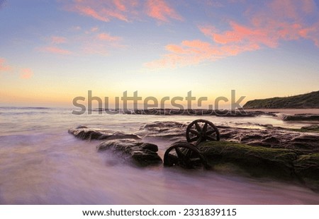 Lovely autumn sunrise over Windang Beach with one of the many abandoned rusty train wheels exposed on mossy rocks at low tide.