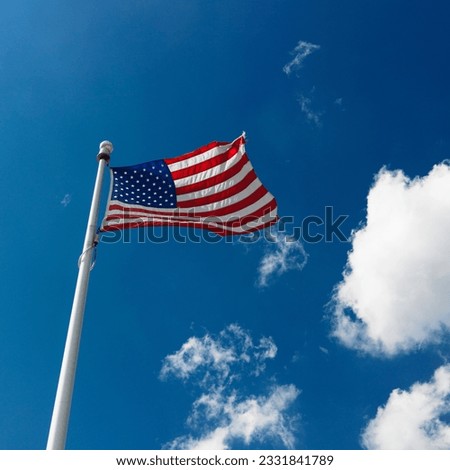 Low angle view of American flag flying with cumulus cloud formation in blue sky.