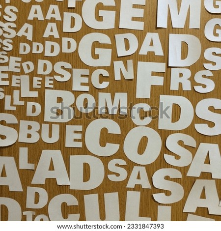 Close up of many white bold paper letters arranged on a wood table