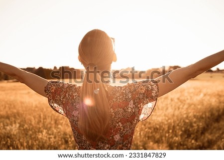 Young woman embraces nature's beauty in a rural, backlit field at sunset. Royalty-Free Stock Photo #2331847829